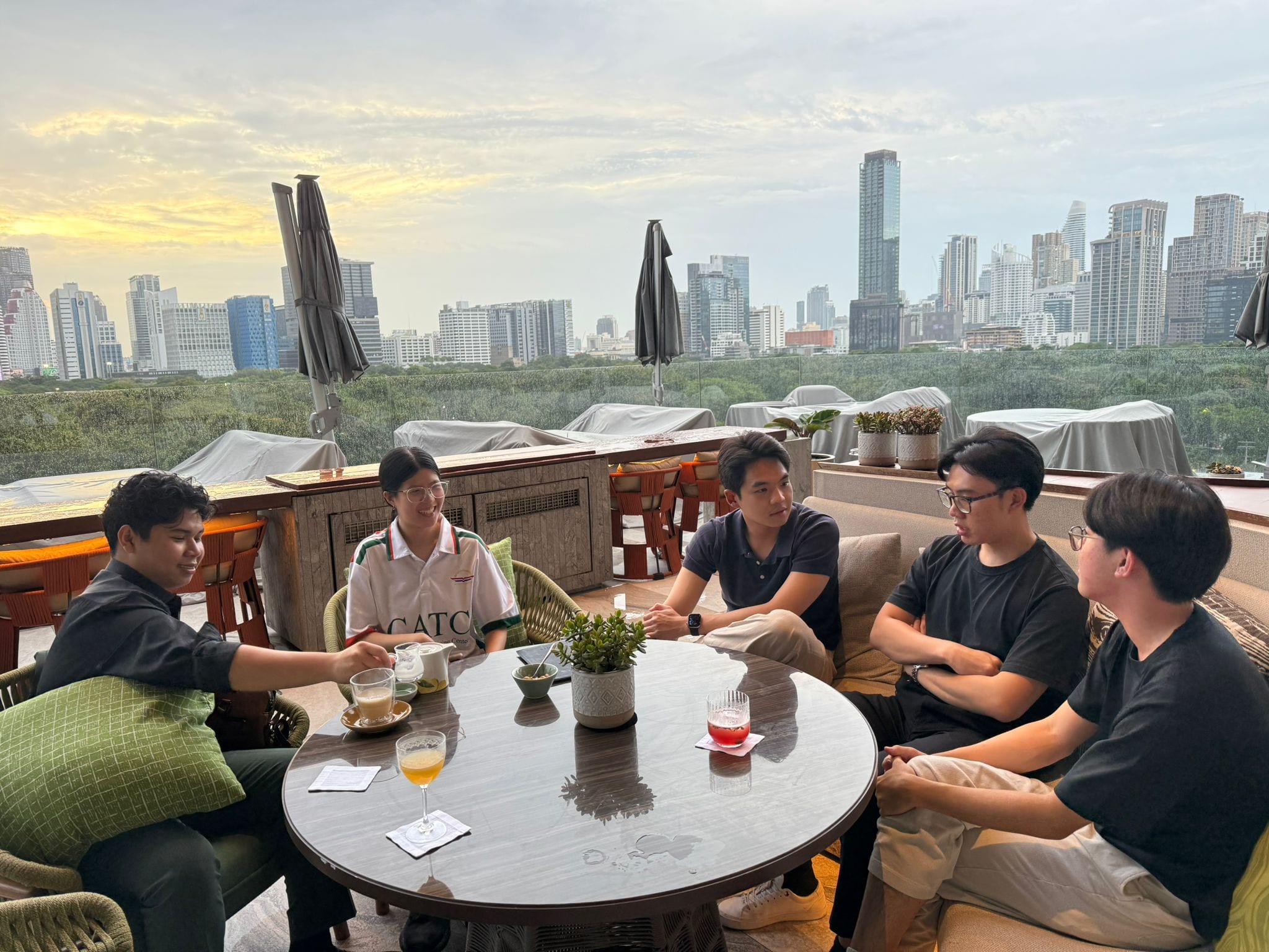 Guests sharing drinks and conversation around a rooftop table at sunset in Bangkok