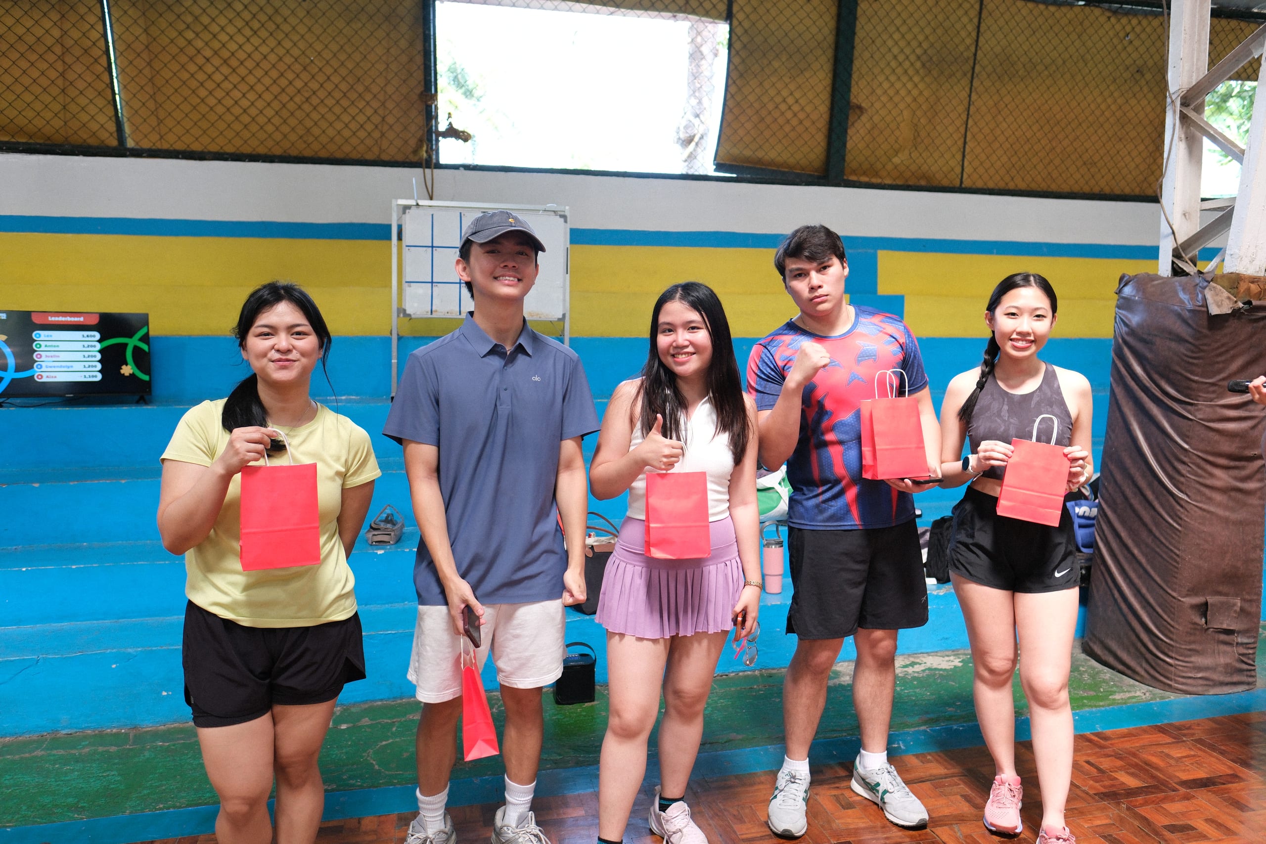 Five participants posing with red gift bags and a paddle