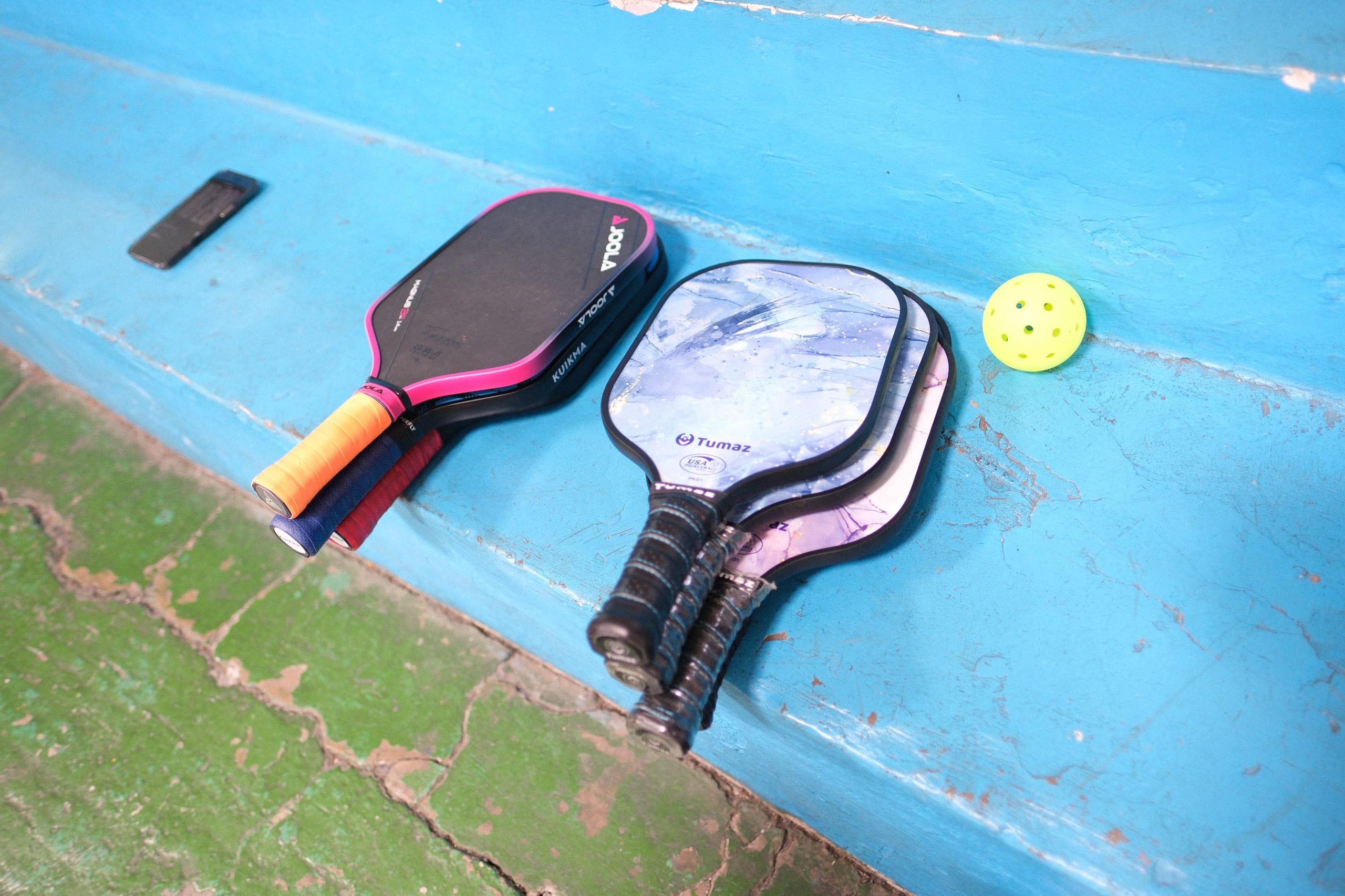 Pickleball paddles and a yellow ball on the blue bleachers